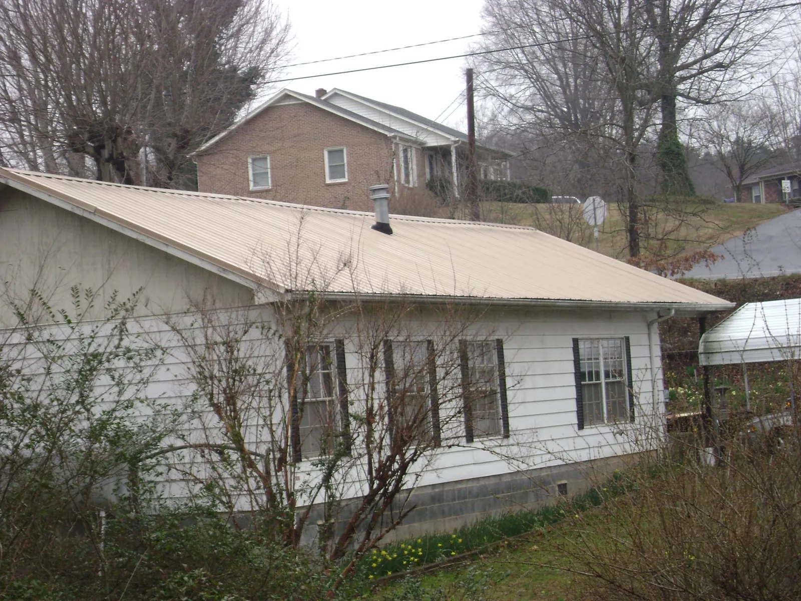 Tan metal roof on a white sided house set into a hillside — Commercial Roofing by Roofing Brothers in Virginia